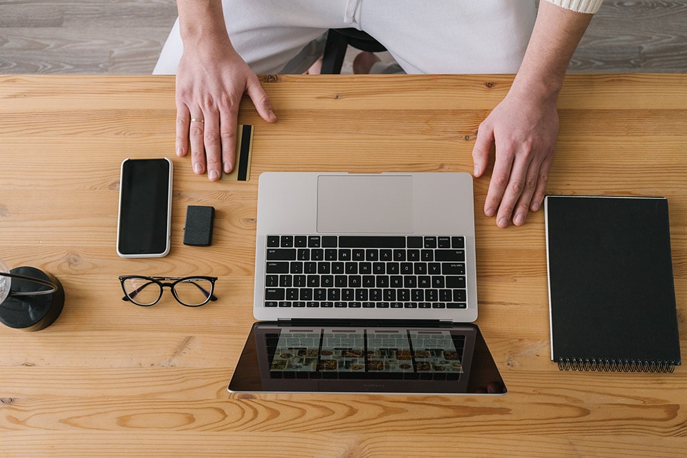 E-biznes: Pan siedzi przed laptopem, na biurku leżą okulary, telefon, notesik oraz karta płatnicza